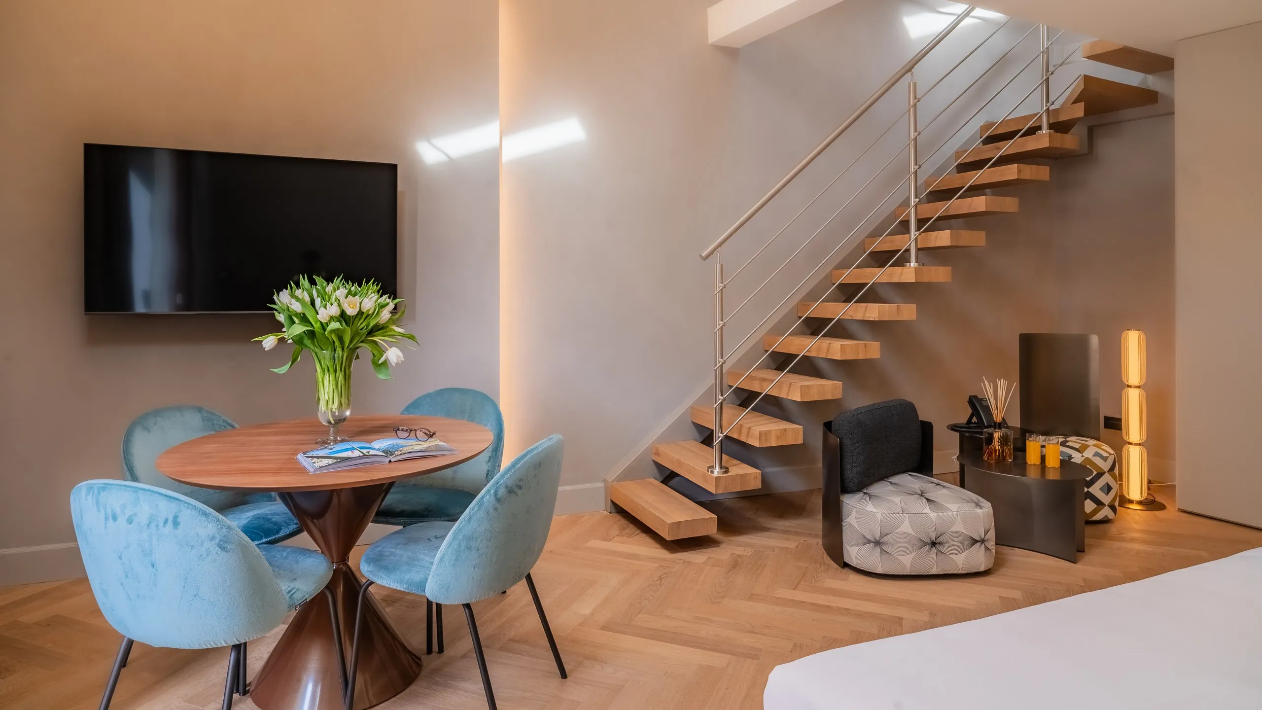 Junior Suite Basil Conrad a Taormina: zona living con tavolo circolare, sedie azzurre e scala moderna in legno.