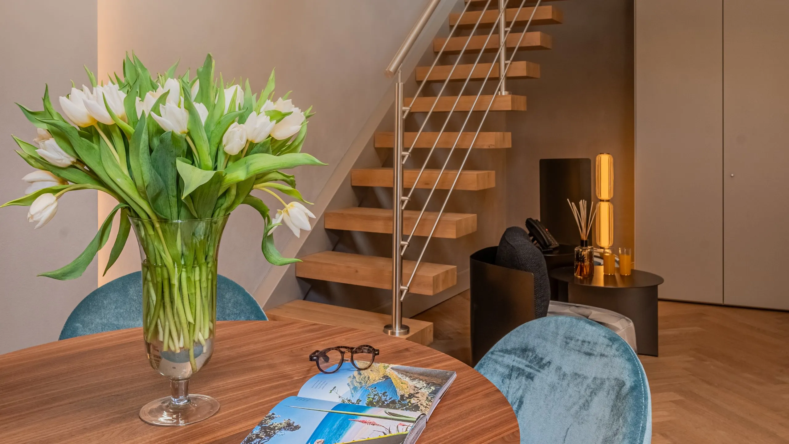 Tavolo in legno con tulipani bianchi, occhiali e scala a sbalzo moderna nella Junior Suite Lord Byron a Villa Conrad.