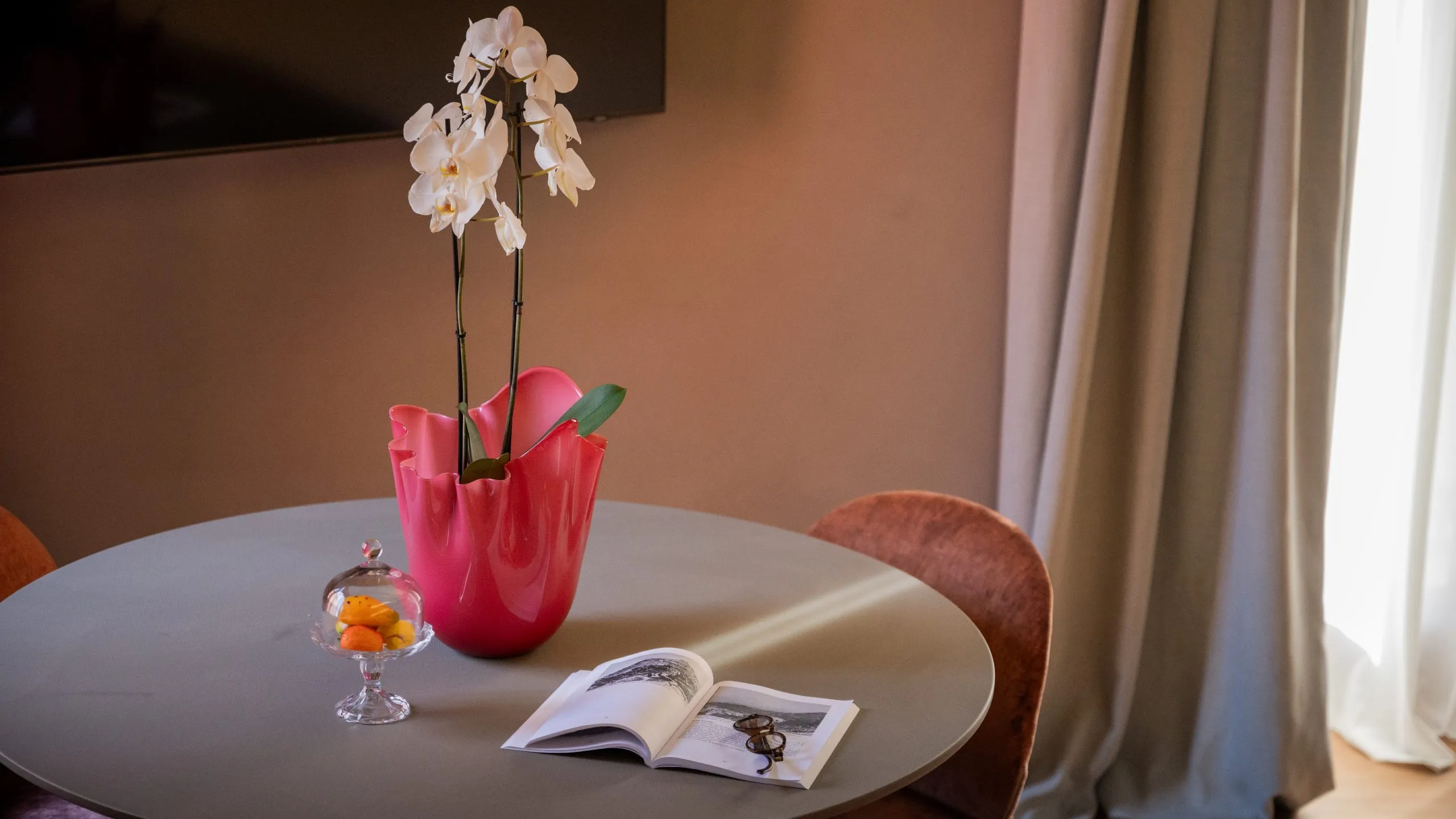 Dettaglio Suite Lady Trevelyan: tavolo di design con orchidea rosa, libro aperto e luce naturale a Villa Conrad.