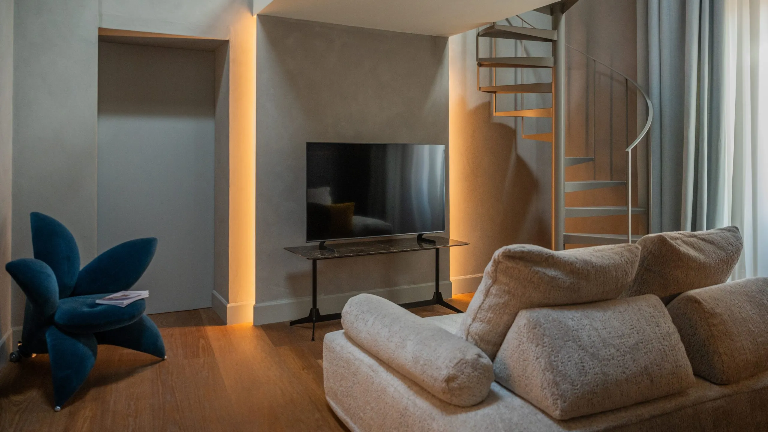 Interni Junior Suite Osbert Sitwell: divano moderno, scala a chiocciola, TV e poltrona blu a Villa Conrad.