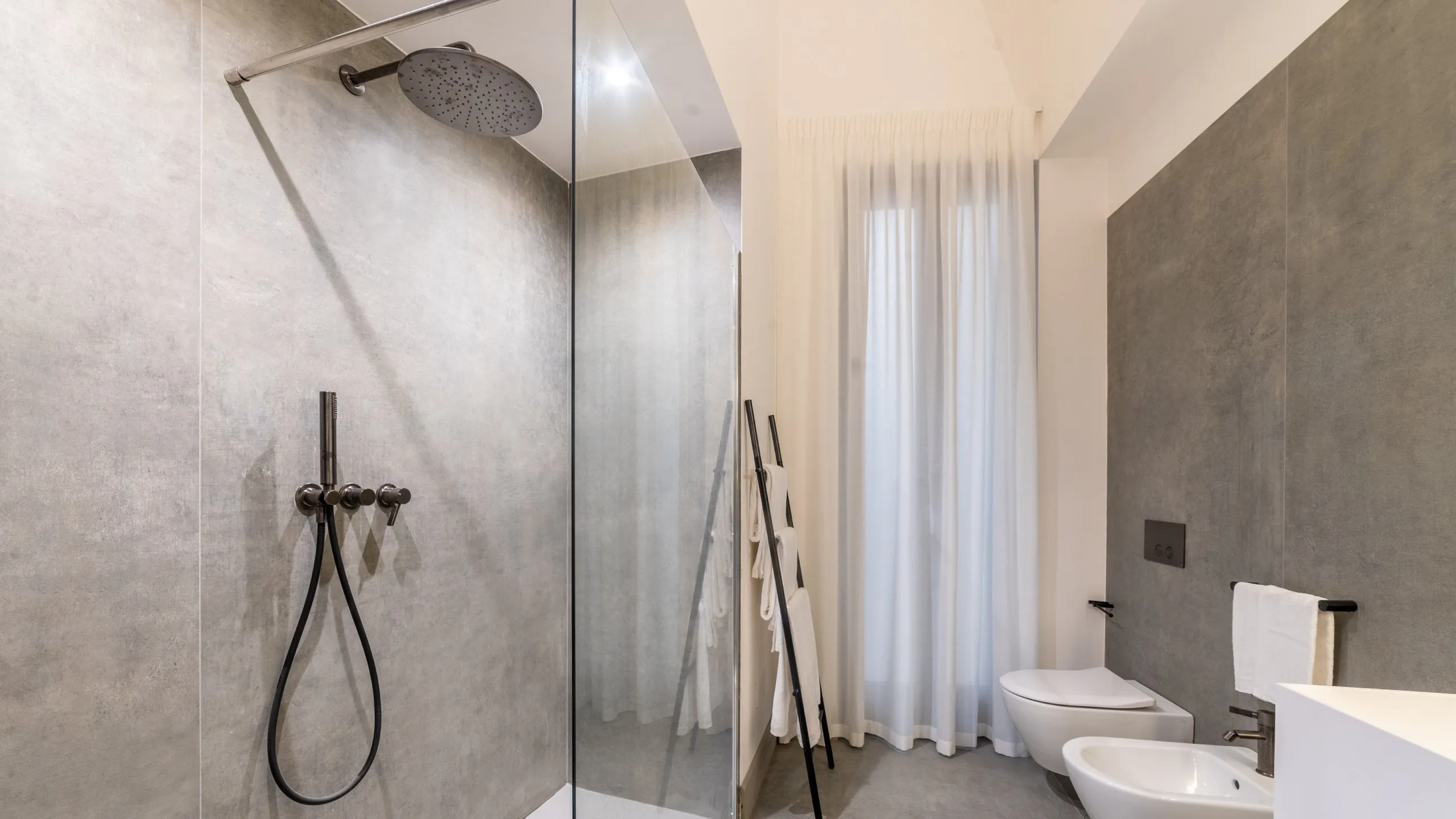 Bagno Junior Suite Villa Conrad: ampia doccia con soffione a pioggia, pareti in resina grigia e sanitari moderni.
