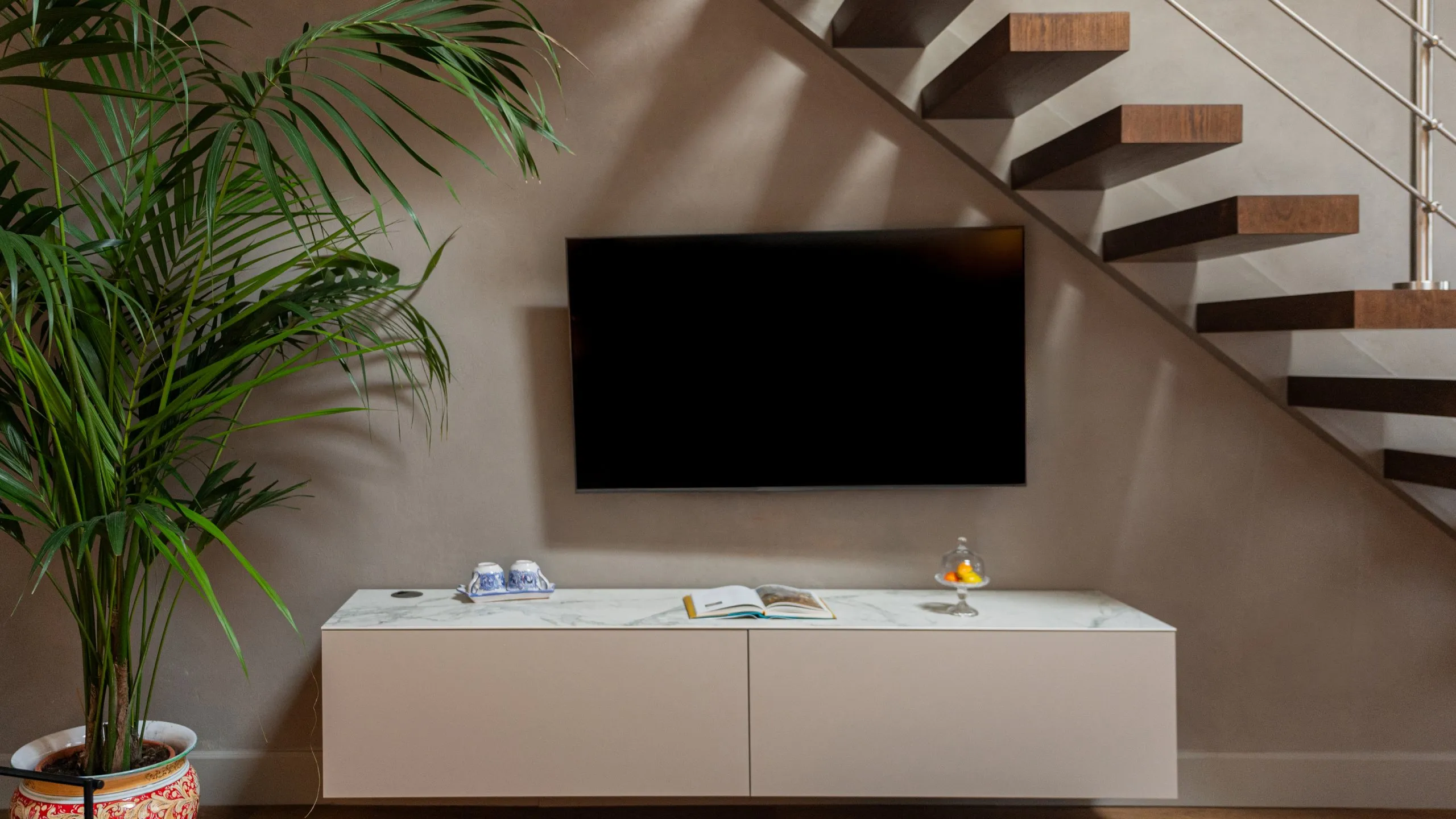 Soggiorno Junior Suite Lord Byron: mobile TV in marmo, scala moderna in legno e pianta esotica a Villa Conrad.