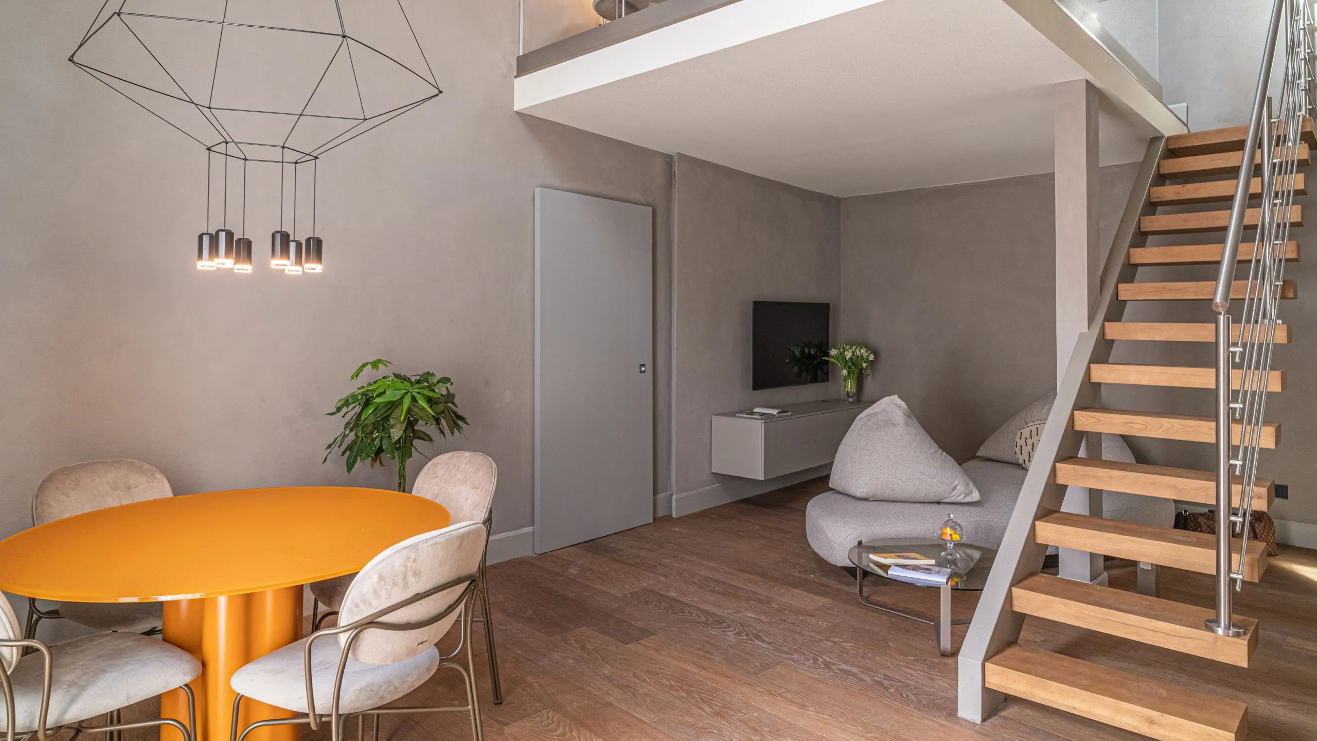 Suite Oscar Wilde: soggiorno open space con tavolo arancio, scala in legno e soppalco di design a Villa Conrad.