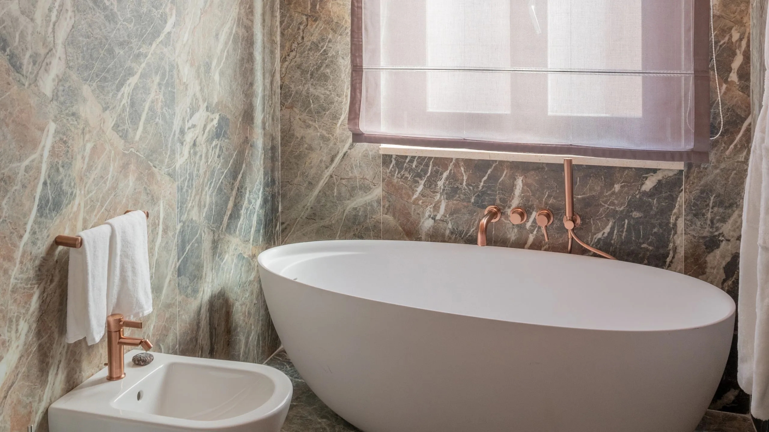 Vasca da bagno a libera installazione in Suite Maupassant con rivestimenti in marmo e dettagli oro rosa.