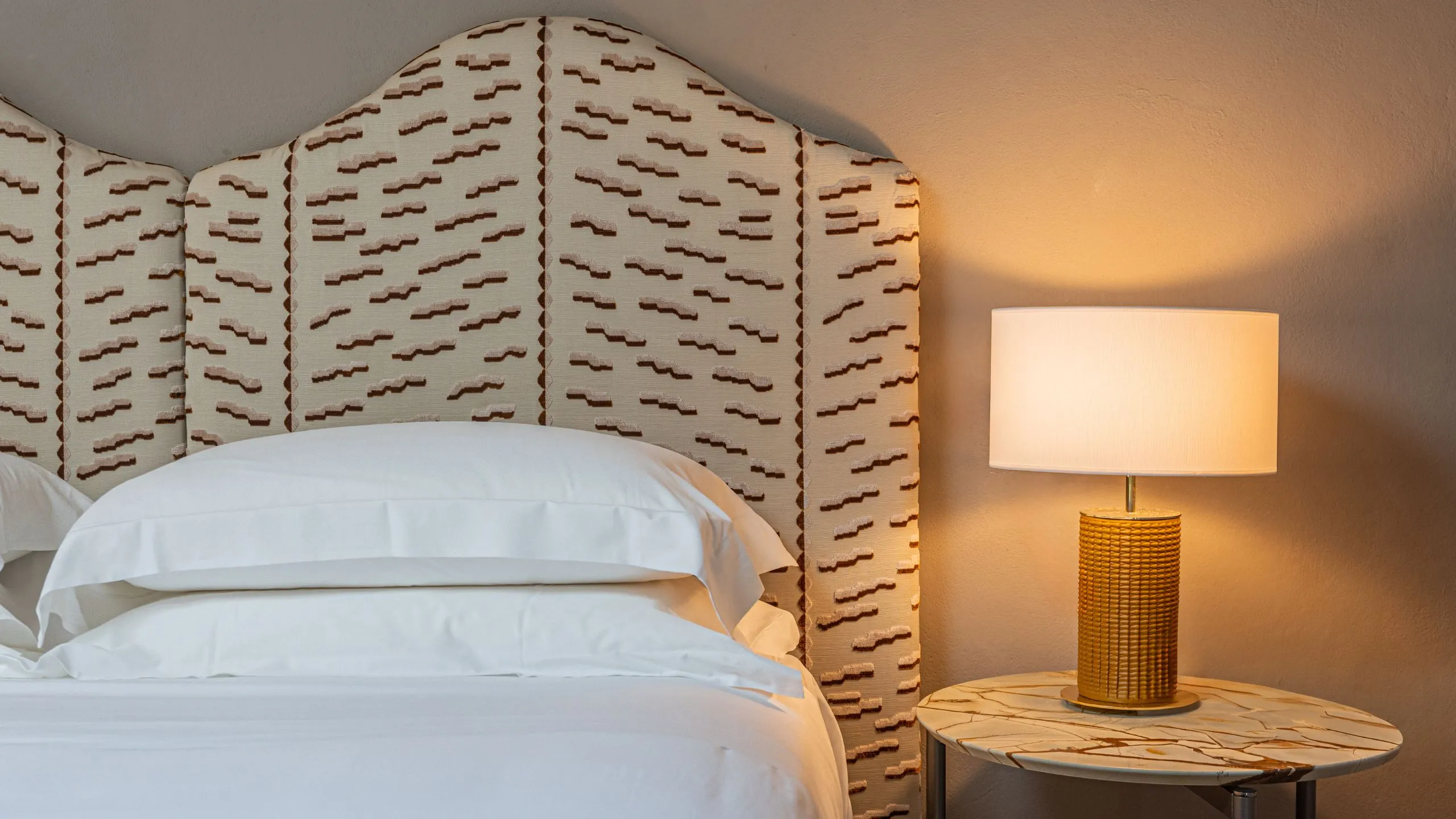 Dettaglio camera Maupassant: testiera letto in tessuto decorato, tavolino in marmo e lampada di design a Villa Conrad.