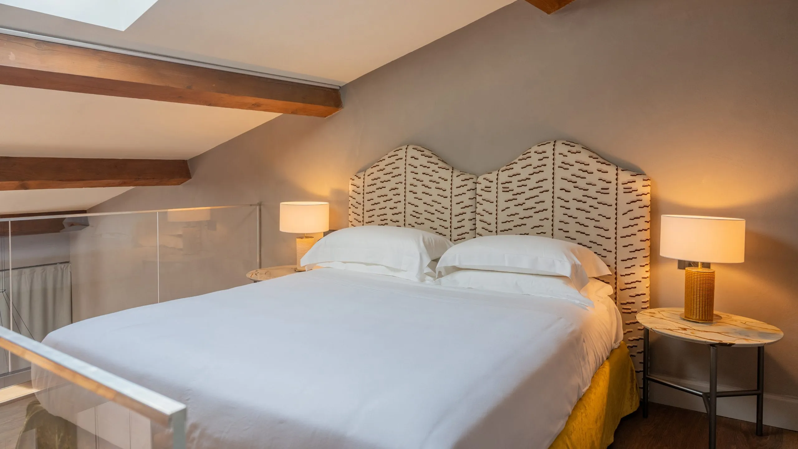 Zona notte Suite Maupassant: letto matrimoniale su soppalco con travi a vista e soffitto mansardato a Villa Conrad.