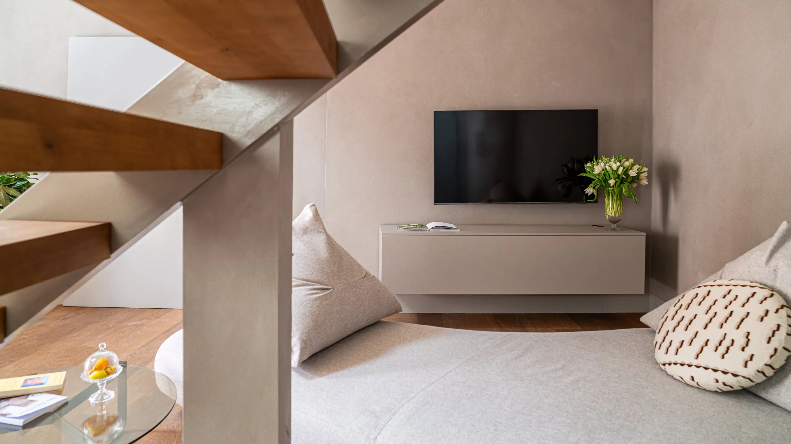 Soggiorno della Suite Oscar Wilde a Villa Conrad: divano curvo grigio, TV a schermo piatto e scala in legno.