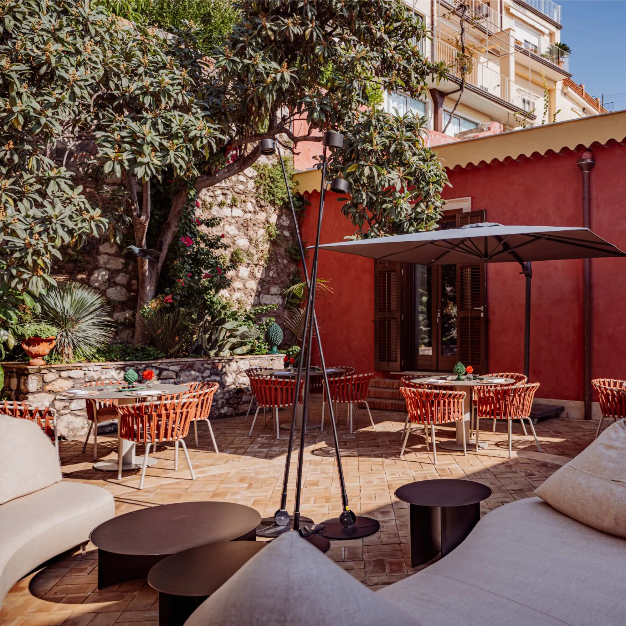 Dehors esterno di Villa Conrad con tavoli di design, sedute eleganti e rigogliosa vegetazione mediterranea a Taormina