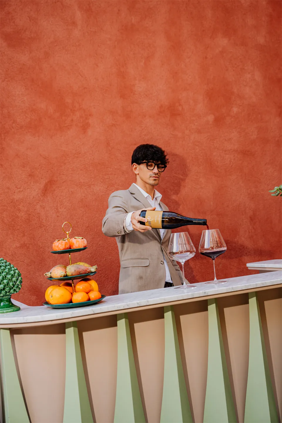 Degustazione vini a Villa Conrad Taormina: sommelier versa vino rosso su bancone di design e parete rossa.