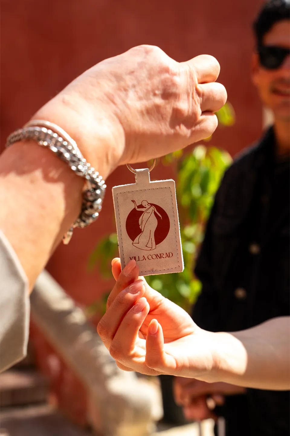 Dettaglio passaggio chiavi a Villa Conrad Taormina: portachiavi in pelle con logo rosso e testo.