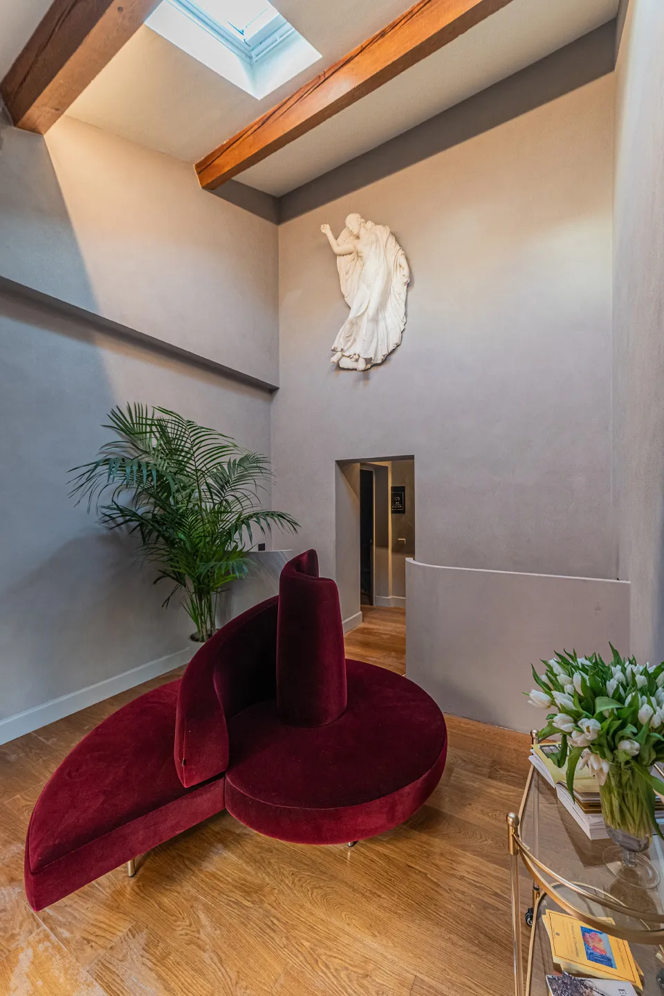 Hall di Villa Conrad a Taormina: divano di design bordeaux, bassorilievo artistico e soffitto con travi in legno.